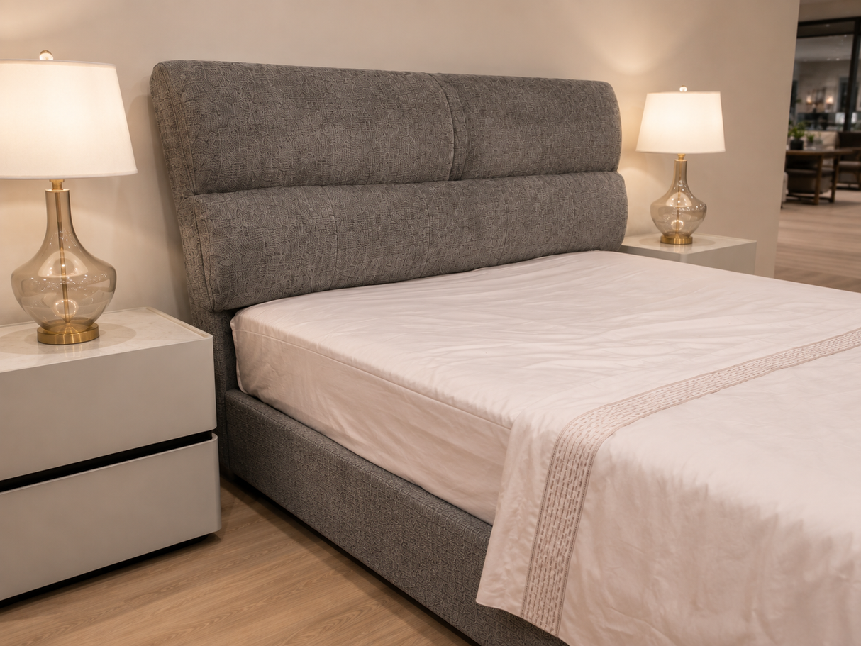 A modern upholstered bed with a tall segmented headboard and matching base, dressed in white bedding, shown in a bedroom setting with two white nightstands and lit table lamps on either side.