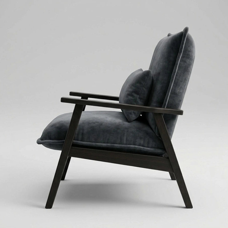 A modern lounge chair with dark charcoal gray velvet cushions and a dark wood frame, shown from a side profile against a light gray studio background.