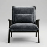 A modern armchair with dark gray velvet upholstery and a matching back cushion, supported by a dark wood frame, shown against a neutral light gray background.