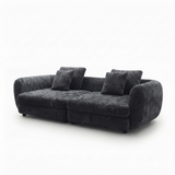 A modern curved three-seater sofa upholstered in dark charcoal gray plush velvet fabric, shown with four matching throw pillows against a plain white background.