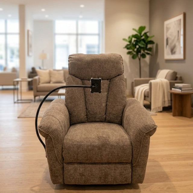 A plush upholstered recliner chair in a warm taupe-brown fabric, shown in a modern living room with wood floors and neutral walls. A black power cord or control cable loops behind the chair.