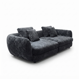 A modern curved three-seater sofa upholstered in dark charcoal gray textured fabric, featuring four matching throw pillows, shown on a plain white background.