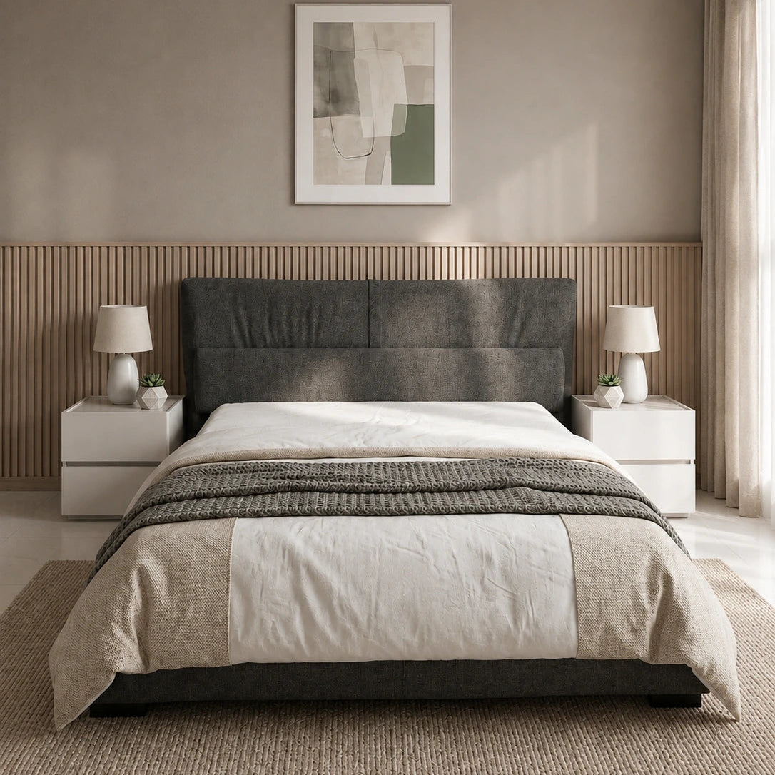 A modern bed with a dark gray upholstered headboard, dressed in white and beige bedding, set in a minimalist bedroom with a slatted wood headboard panel, bedside tables, lamps, and a textured rug.
