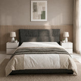 A modern bed with a dark gray upholstered headboard, dressed in white and beige bedding, set in a minimalist bedroom with a slatted wood headboard panel, bedside tables, lamps, and a textured rug.