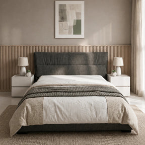 A modern bed with a dark gray upholstered headboard, dressed in white and beige bedding, set in a minimalist bedroom with a slatted wood headboard panel, bedside tables, lamps, and a textured rug.